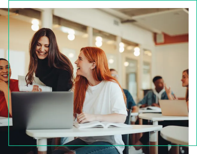 Zwei Frauen unterhalten sich vor einem Laptop in einer Cafeteria